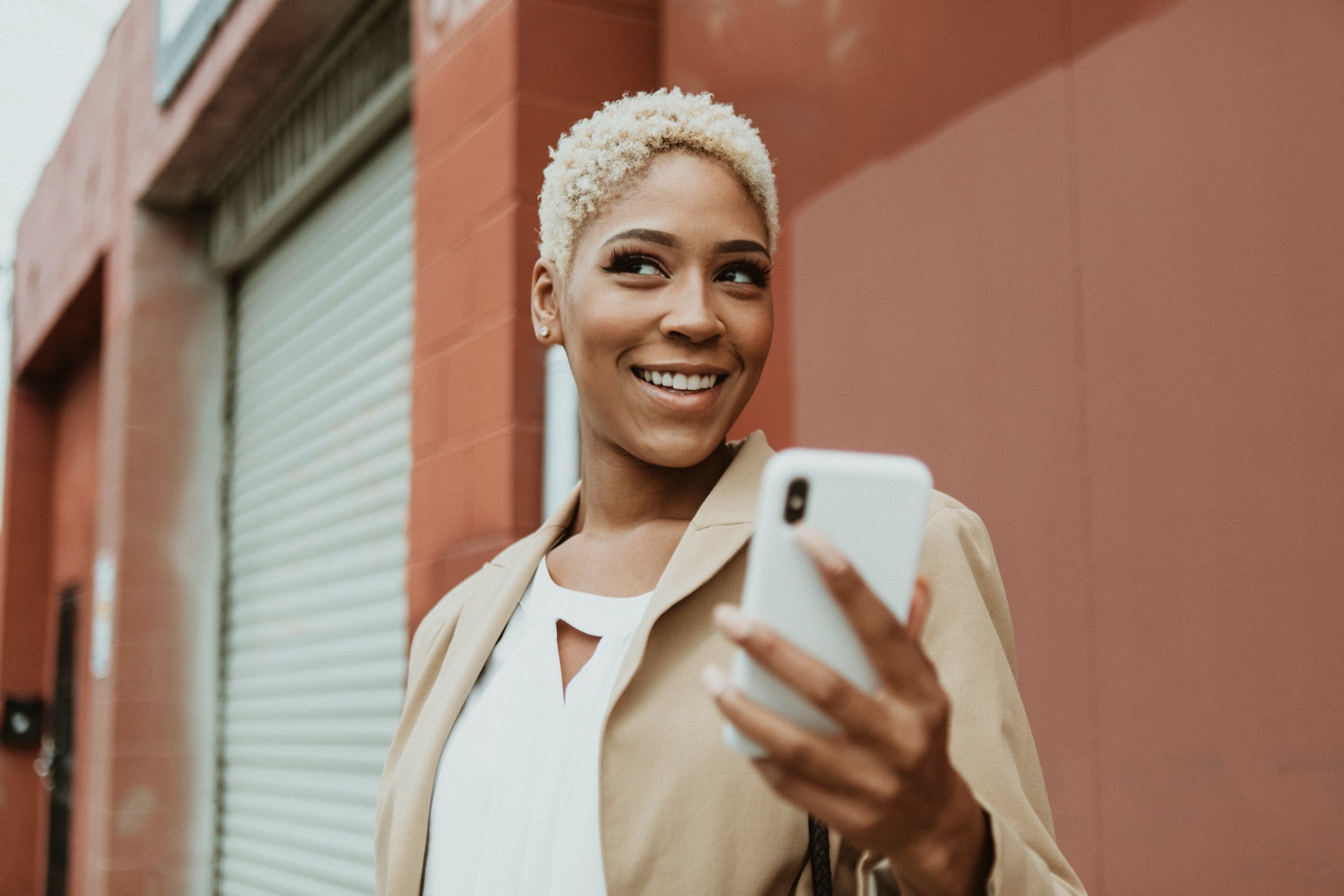 Woman smiling at her phone by a terracotta wall