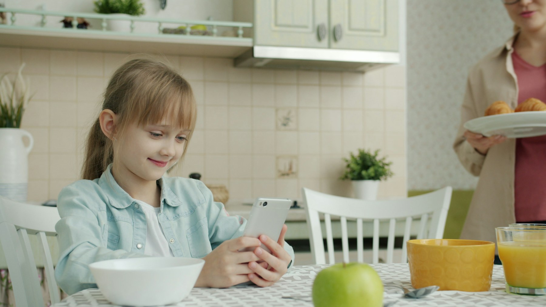 A girl using a phone at the kitchen table at breakfast