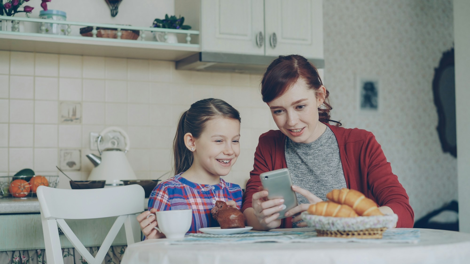 A mother and daughter share a phone at the kitchen table