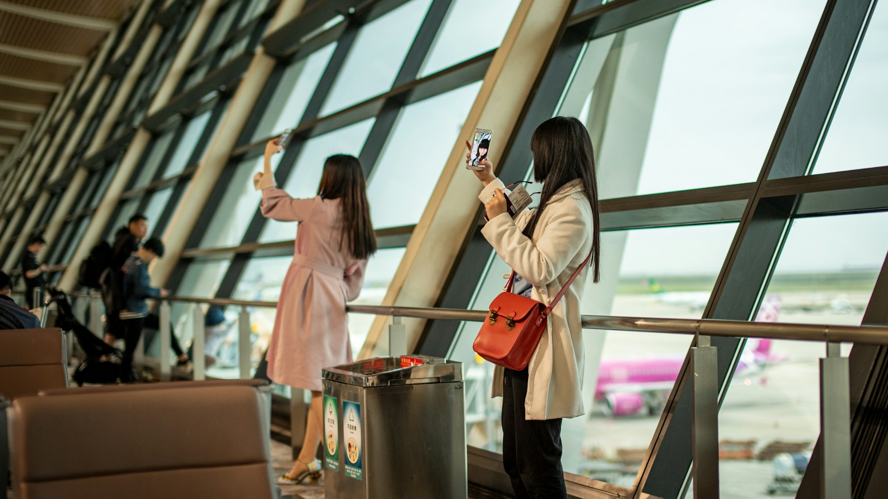 Two travelers taking photos by an airport window